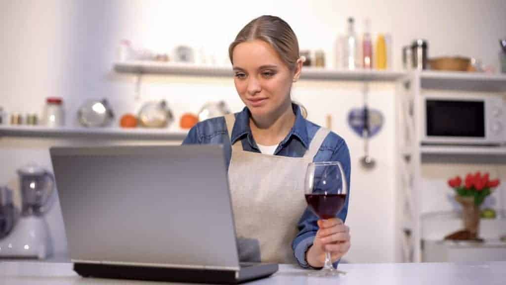 Winery marketer holding a wine glass in front of her laptop as she designs a winery website